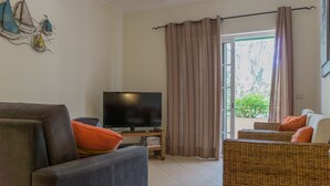 A living room with a flat-screen TV, wicker furniture, and a window with curtains.