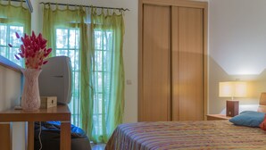 A bedroom with a bed, a desk with a computer, a lamp, and a window with curtains.