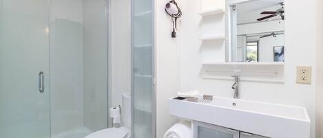 Ein modernes Badezimmer mit Duschkabine aus Glas, Toilette in Weiß, Waschbecken mit Spiegel und Deckenventilator.