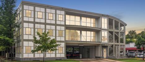 Un edificio moderno con tejado plano, amplios ventanales y un área de estacionamiento techada.