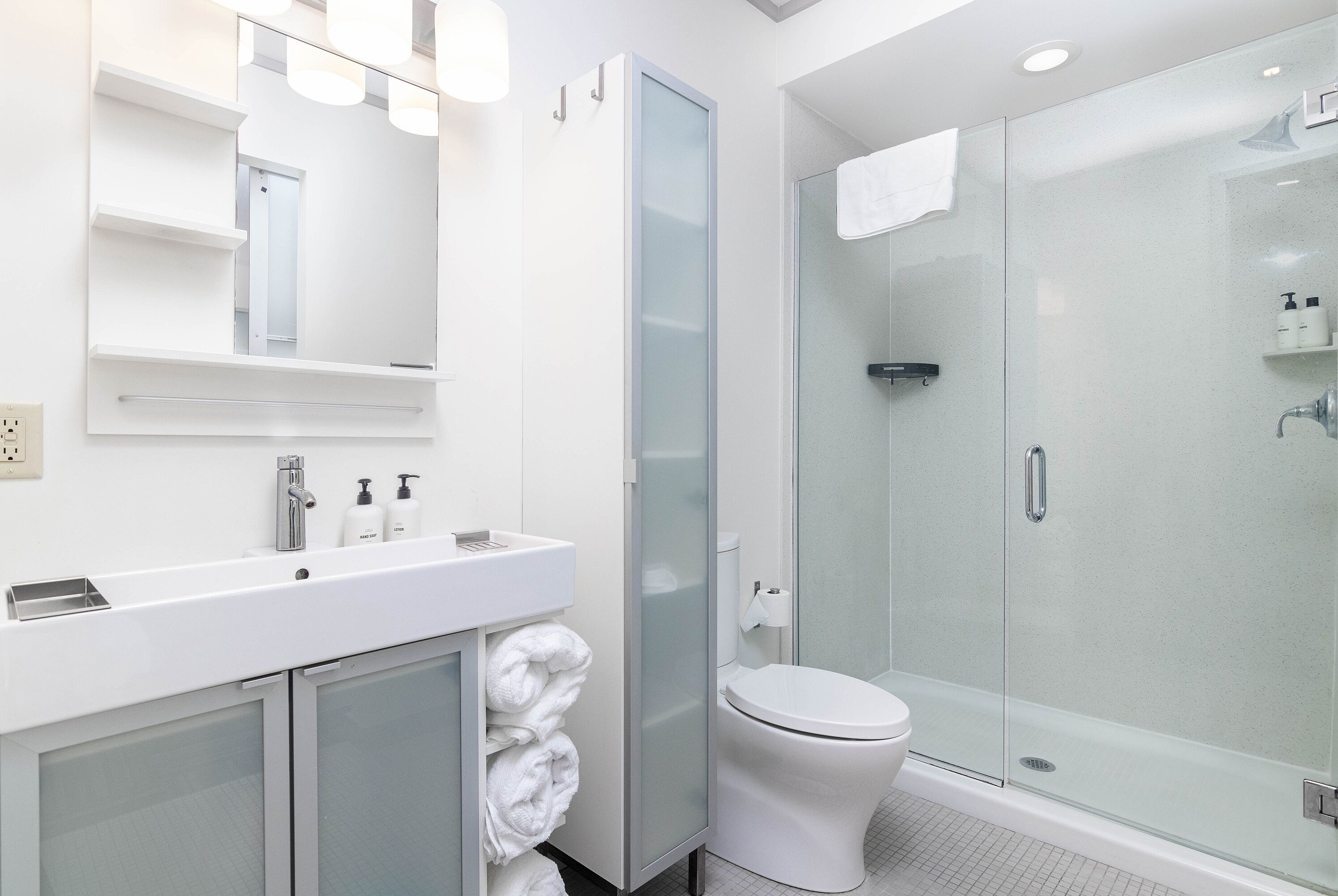 Un baño moderno con cabina de ducha de vidrio, un lavabo blanco con espejo y un inodoro.