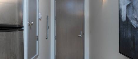 Un couloir étroit doté d’un plancher en bois, une porte fermée, un luminaire fixé au mur et un grand tableau abstrait.