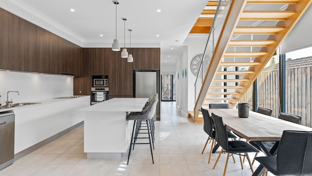 A modern kitchen with a central island, a dining area with a wooden staircase, and a view of the outside. - North Entrance Holiday Home (North Entrance)
