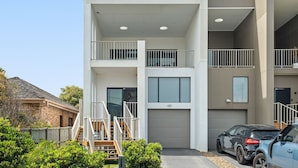 A modern multi-story residential building with a garage, a staircase, and a carport with two cars. - North Entrance Holiday Home (North Entrance)