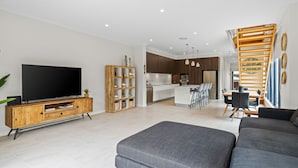 A modern living room with a flat-screen TV, a wooden entertainment unit, a grey sofa, and a kitchen in the background. - North Entrance Holiday Home (North Entrance)