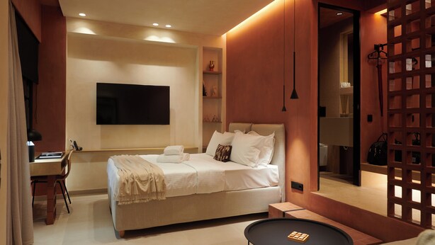 A modern bedroom with a bed, bedside table, and a TV mounted on the wall. - K23 Color Suites (Athens)