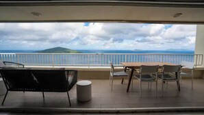 Ein Balkon mit Tisch und Stühlen, einem Mülleimer und Blick auf das Meer und eine entfernte Insel.