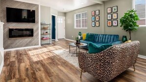 Een woonkamer met een blauwe bank, een fauteuil met luipaardprint, een flatscreen televisie en een open haard.