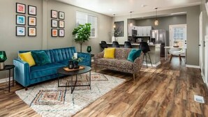 Een ruime woonkamer met een blauwe bank en een gestreept fauteuil, een bijzettafeltje en een vloerkleed.