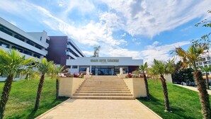 The Grand Hotel Caraiman with a modern facade, a central staircase leading to the entrance, and palm trees in the foreground. - Grand Hotel Caraiman (Neptun)