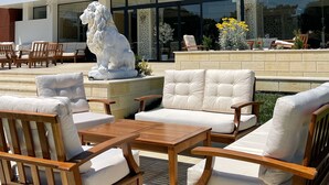 The exterior of Grand Hotel Caraman with a white facade, a large lion statue, and outdoor seating area with wooden furniture. - Grand Hotel Caraiman (Neptun)