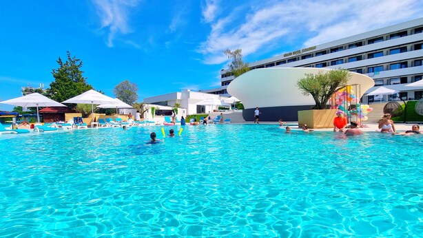A large outdoor swimming pool with clear blue water, surrounded by lounge chairs and umbrellas. - Grand Hotel Caraiman (Neptun)