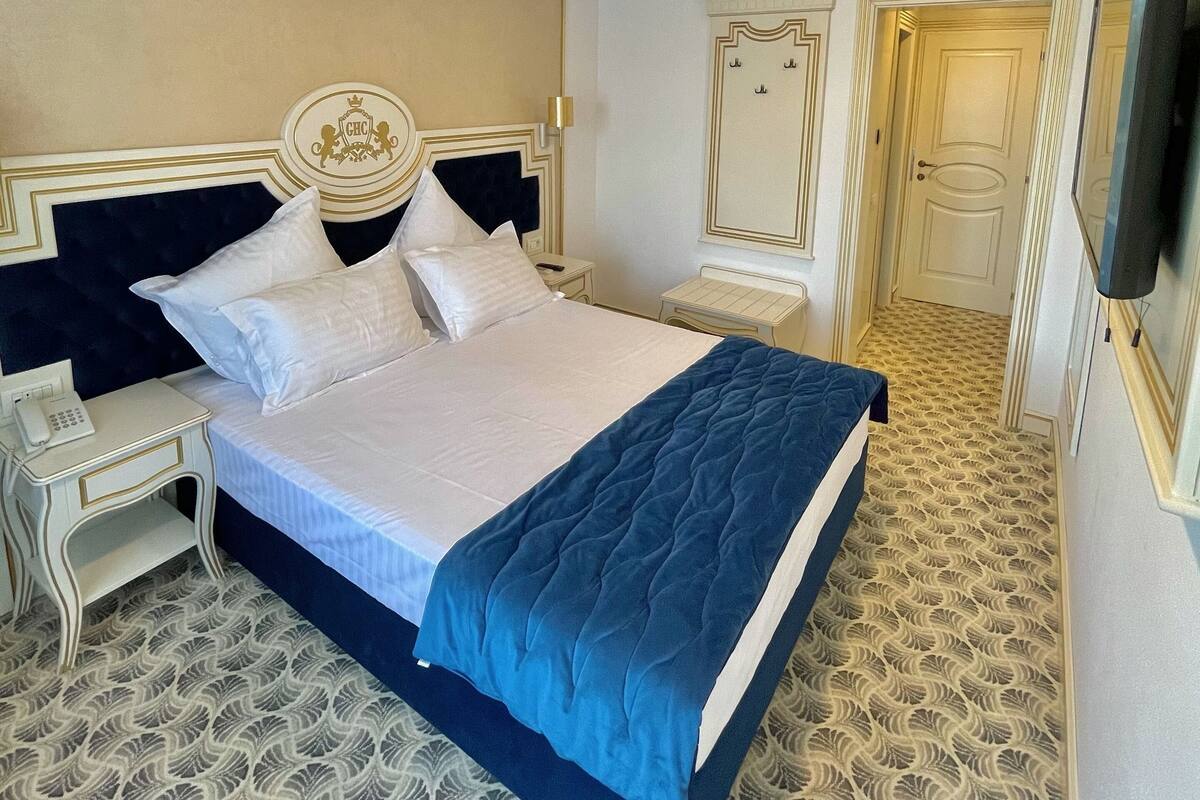 A hotel room with a large bed, bedside tables, a telephone, and a television.