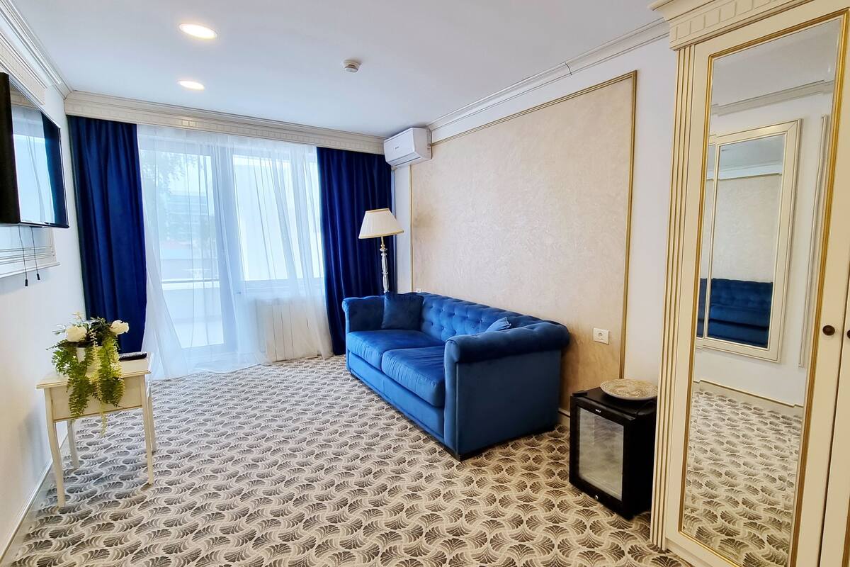 A hotel room with a blue sofa, patterned carpet, a mirror, and a large wardrobe.