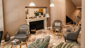 A living room with patterned armchairs, a glass coffee table, a fireplace, and pendant lighting. - HOTEL SAHAT (Sarajevo)