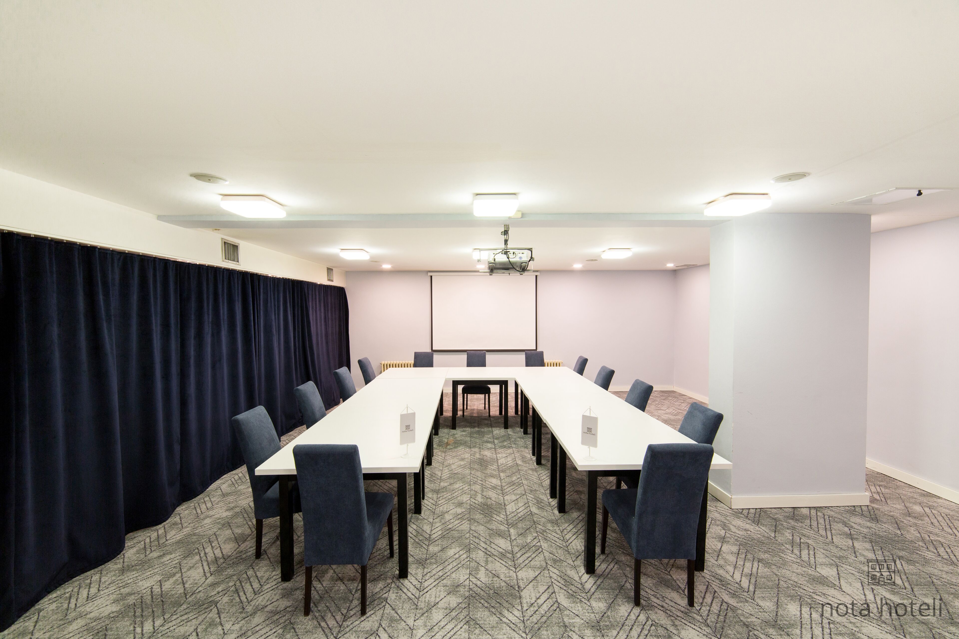 A conference room with a long table, chairs, a projector screen, and a dark curtain.
