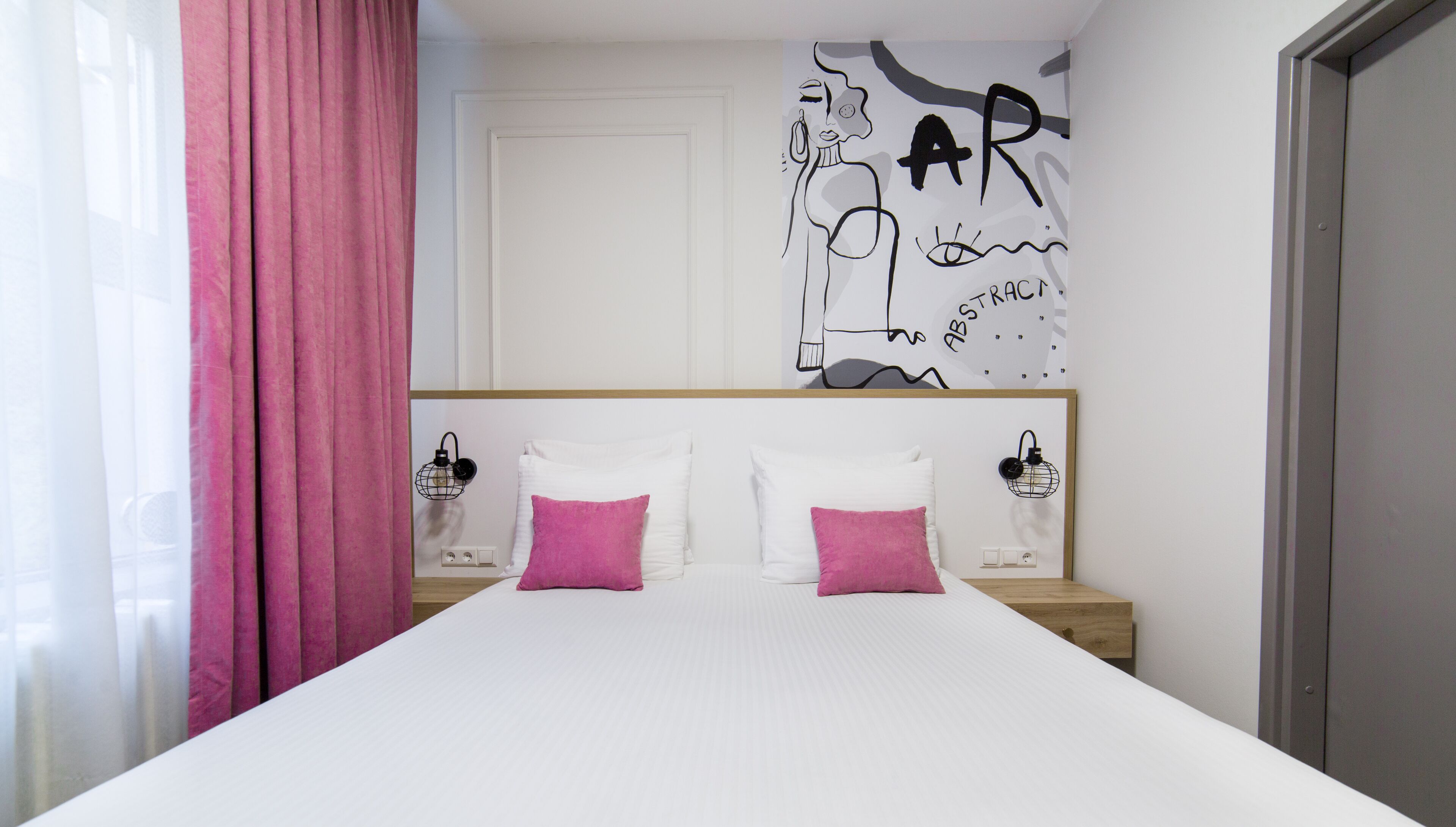 A bedroom with a bed, two bedside tables, a headboard, a pink curtain, and a wall with a graphic.