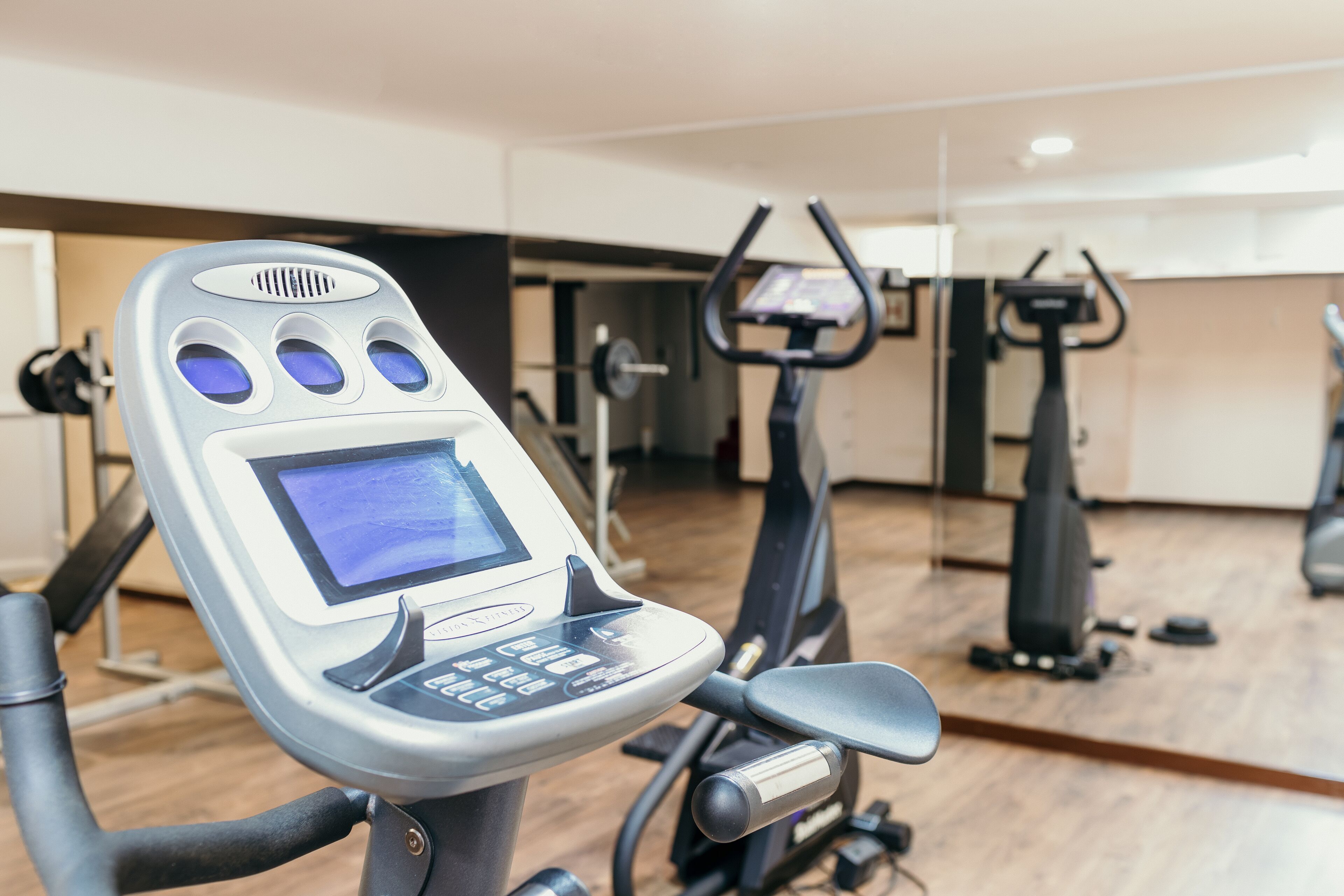 A stationary bike with a digital display and control panel, in a gym with a mirror wall and other exercise equipment.