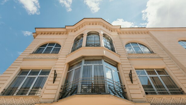 A multi-story building with a symmetrical facade, large windows, and a balcony with a metal railing. - HOTEL SAHAT (Sarajevo)