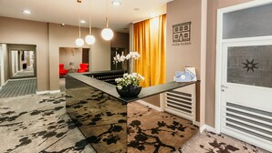 A hotel reception area with a modern design, including a reception desk, a large mirror, and a seating area with red chairs. - HOTEL SAHAT (Sarajevo)
