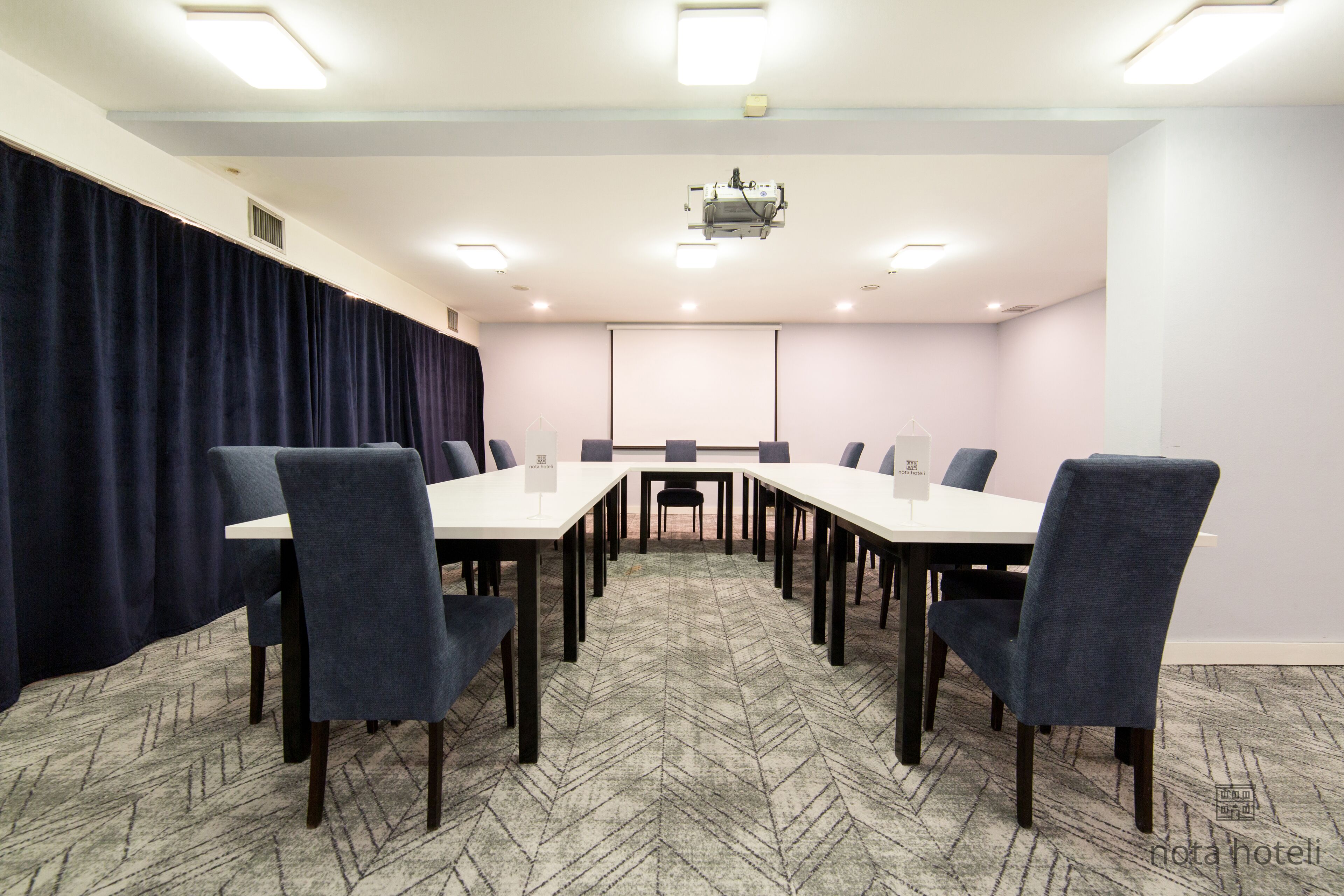 Une salle de conférence avec une longue table, des chaises, un écran de projection et un sol recouvert de moquette.
