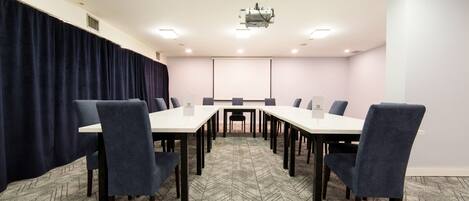 Une salle de conférence avec une longue table, des chaises, un écran de projection et un sol recouvert de moquette.