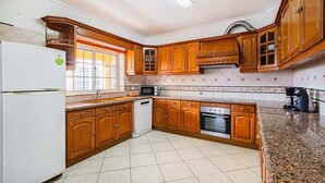 A kitchen with wooden cabinets, a refrigerator, a microwave, a dishwasher, and a stove. - Villa Coelha - Table tennis and Pool Table (Guia)