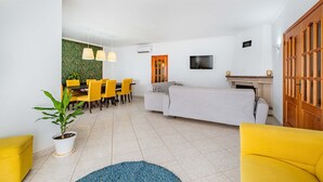 A living room with a sofa, yellow chairs, a dining table, and a TV. - Villa Coelha - Table tennis and Pool Table (Guia)