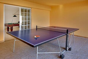 A ping pong table with a ball in the center, a billiards table, and a door in the background. - Villa Coelha - Table tennis and Pool Table (Guia)