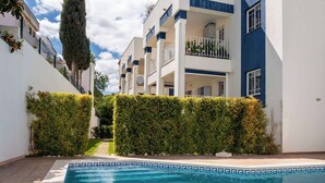 A swimming pool with a geometric tile border, surrounded by neatly trimmed hedges and modern buildings with balconies. - Apartment Claro Azul (Albufeira)