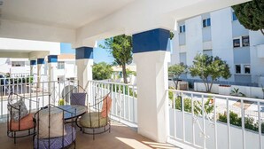 A balcony with a table and chairs, white railings, and a view of neighboring buildings and trees. - Apartment Claro Azul (Albufeira)