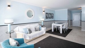 A modern living room with a white sofa, a blue armchair, a dining table with chairs, and a black rug. - Apartment Claro Azul (Albufeira)