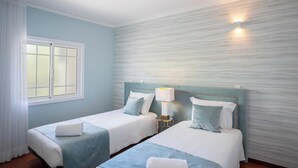 A hotel room with two beds, a window with white curtains, a wall-mounted light, and a nightstand with a lamp. - Apartment Claro Azul (Albufeira)