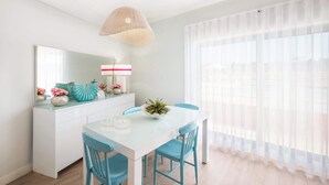 A bright dining area with a white table, blue chairs, a woven pendant light, and a large window with sheer curtains. - Al Marina View Uma - Lux ground floor apartment on the marina (Albufeira)