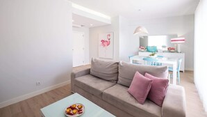 A modern living room with a beige sofa, a light blue coffee table, and a dining area with a white table and blue chairs. - Al Marina View Uma - Lux ground floor apartment on the marina (Albufeira)
