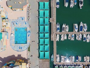 An aerial view of a marina with boats docked, a swimming pool, and a covered walkway.