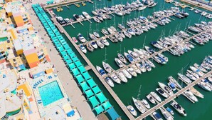 An aerial view of a marina with numerous boats docked in a grid pattern, a swimming pool, and colorful buildings with balconies. - Al Marina View Uma - Lux ground floor apartment on the marina (Albufeira)