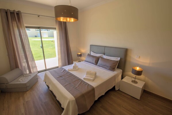 A bedroom with a large bed, bedside lamps, a sofa, and a view of the outdoors.
