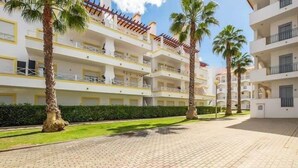 Un hotel a più piani con balconi, palme e un cortile lastricato.