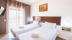 Una camera d'albergo con due letti, una televisione, un quadro e una finestra con tende.
