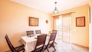 Zona pranzo con tavolo apparecchiato per quattro, sedie in legno, lampadario a sospensione e due opere d'arte incorniciate alle pareti.