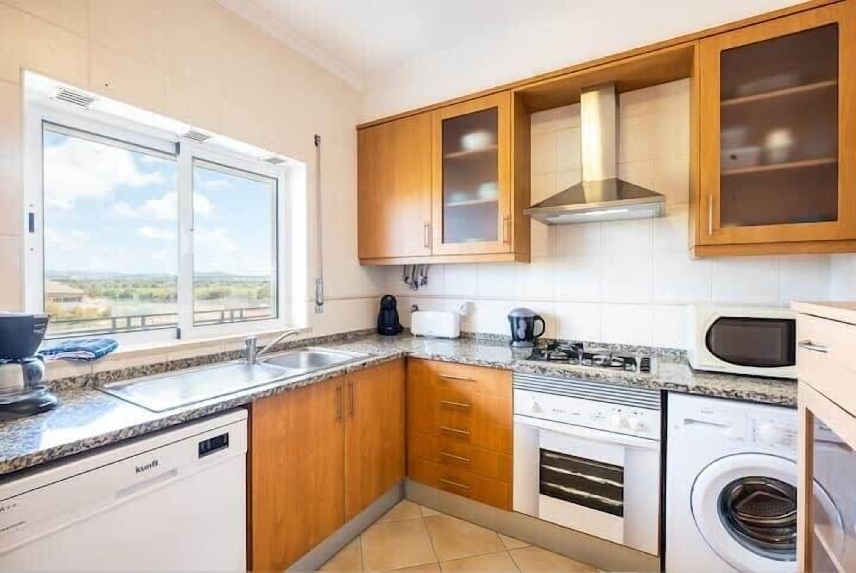 Eine moderne Küche mit Holzausstattung, integriertem Backofen, Waschmaschine und einem Fenster mit Aussicht.