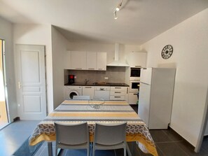 Eine kompakte Küche mit Essbereich, darunter ein Tisch mit Stühlen, eine Waschmaschine, eine Mikrowelle und ein Kühlschrank.