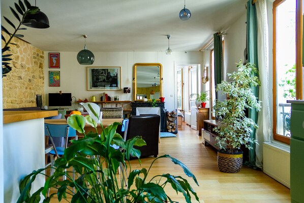 Relax in this inviting living room with a comfortable sofa, dining table, and chair, plus a large mirror and potted plants.