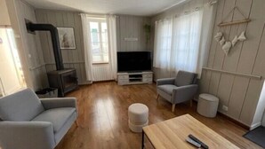 A living room with a sofa, armchair, ottoman, wooden coffee table, TV, and a fireplace. - House in the center, near the beach (Rivedoux-Plage)