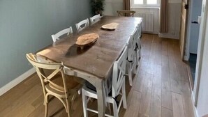 A dining area with a long wooden table, white chairs, a wall clock, and a hanging light fixture. - House in the center, near the beach (Rivedoux-Plage)