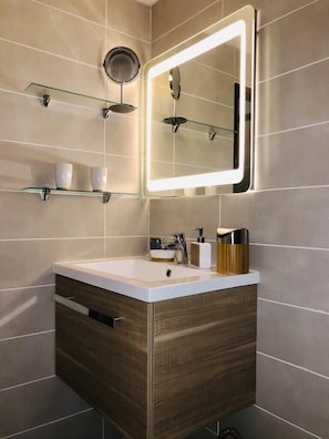 Een moderne badkamer met een wastafel, een spiegel met ingebouwde verlichting en een plank met bekers.