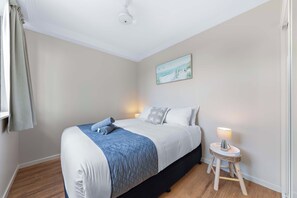 Quarto com cama, mesa de cabeceira, luminária e um quadro na parede.