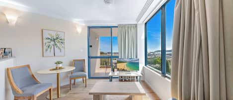 A modern living room with a large window, a ceiling fan, and a view of a beach.
