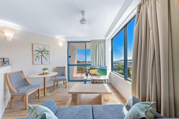 A modern living room with a large window, a ceiling fan, and a view of a beach.